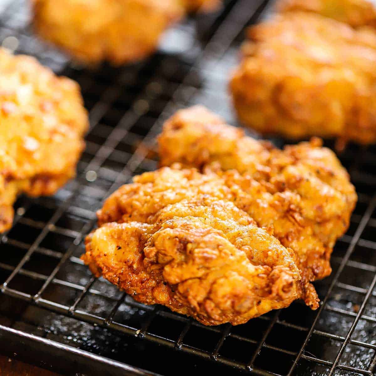 Several rows of crispy fried chicken thighs resting on a baking rack nestled into a baking pan.