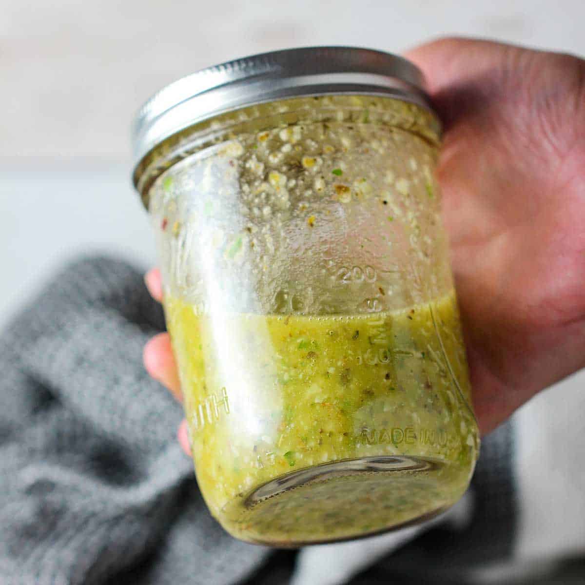 A person holding a jar of homemade Italian dressing with a lid screwed on and has just been vigorously shaken.
