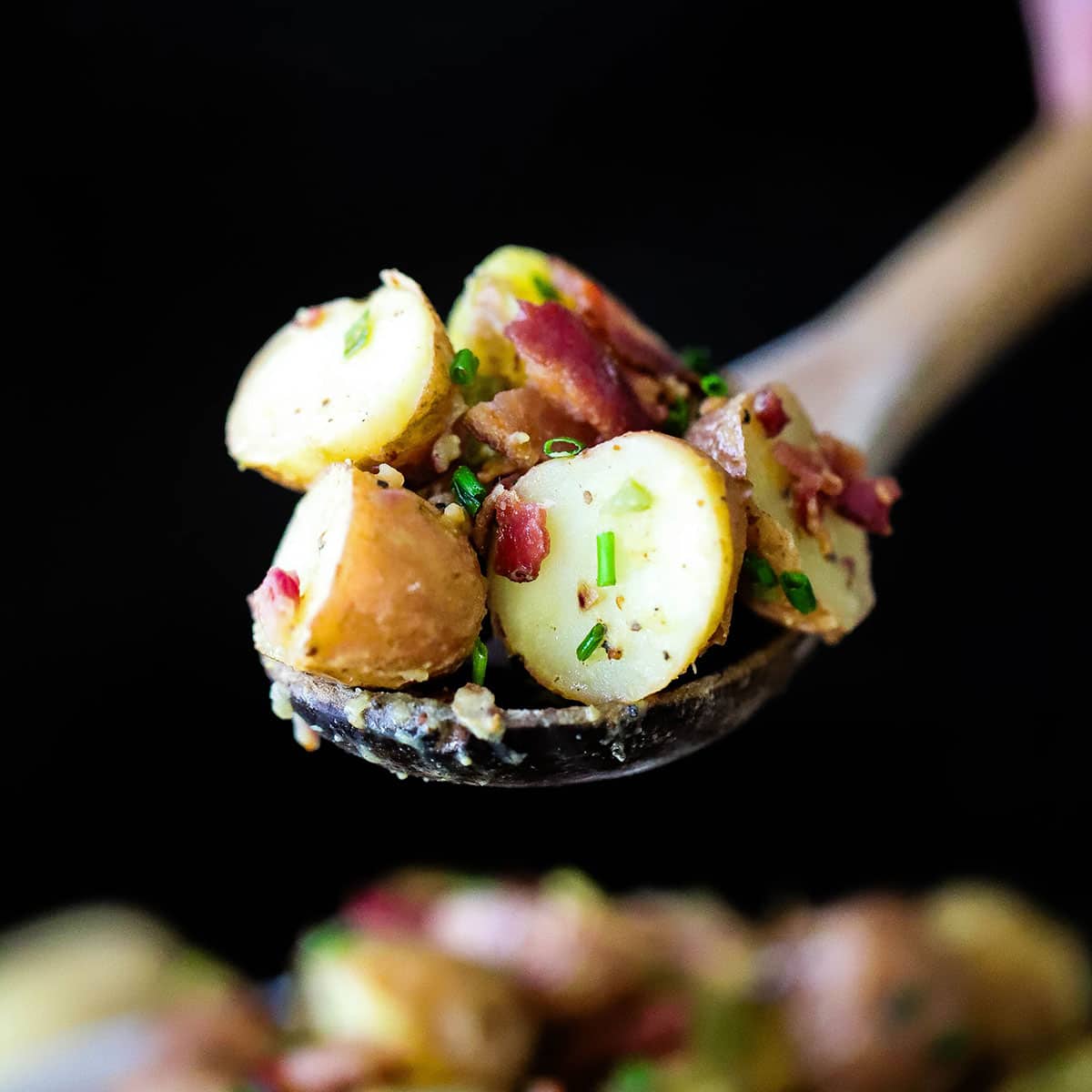 A person holding up a wooden spoon that is holding a serving of Best German Potato Salad.
