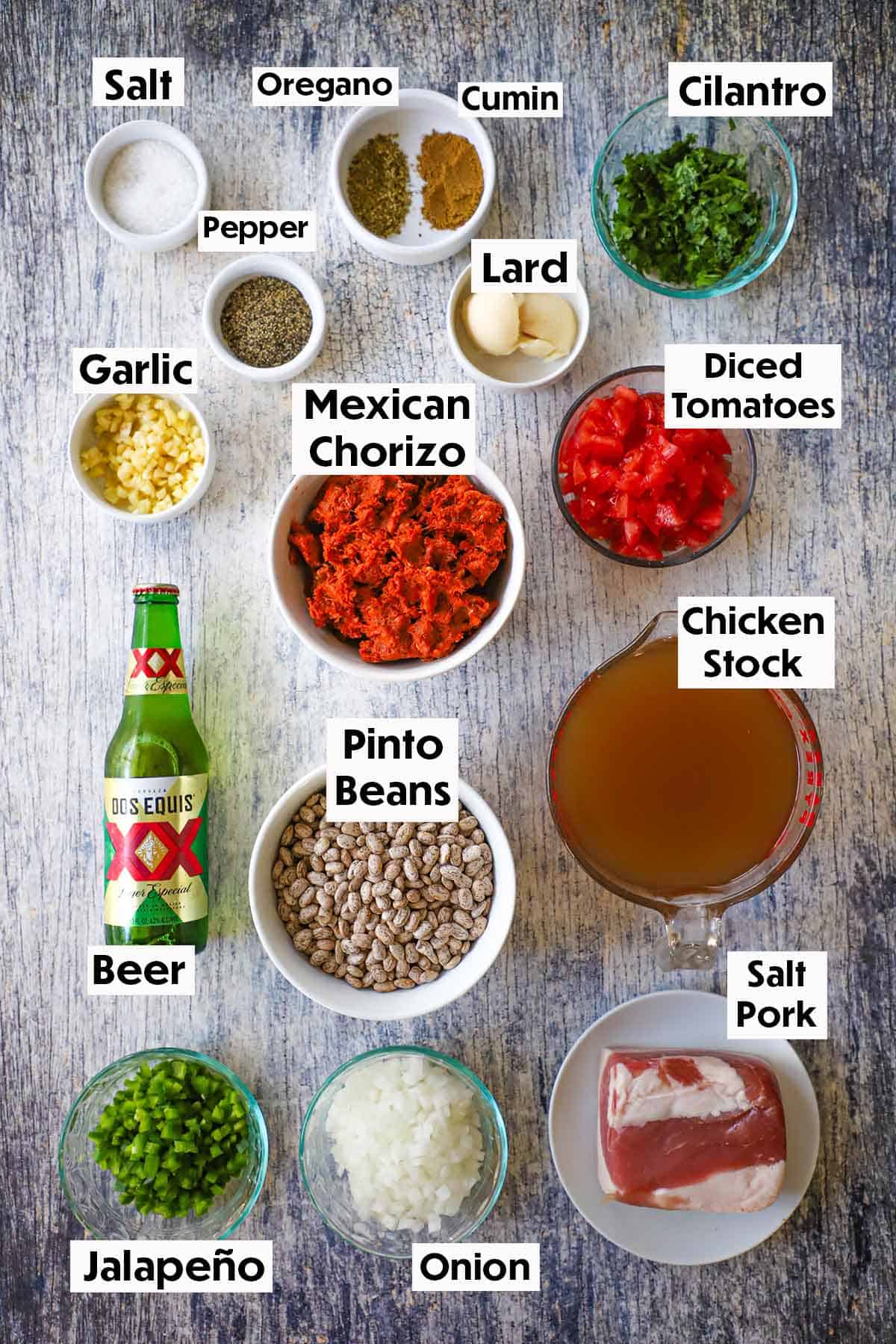 An arrangement of ingredients for chorizo and bean soup including Mexican chorizo, pinto beans, salt pork, chicken stock, a bottle of beer, chopped onions and jalapeños, garlic, and seasonings.