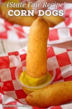 A person plunging a homemade corn dog into a small plastic container filled with yellow mustard.
