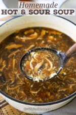 A person using a large wooden ladle to transfer homemade Chinese hot and sour soup from a large pot into a festive Asian soup bowl.