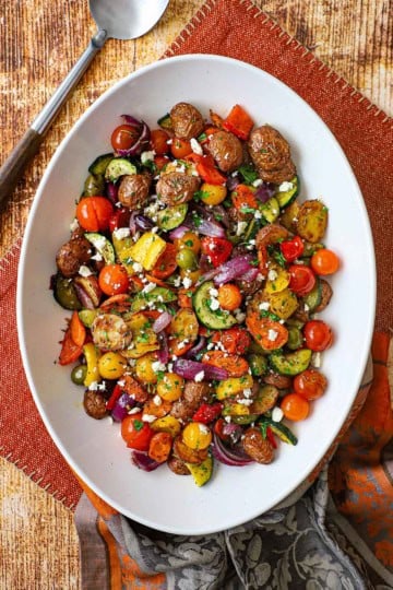 A large white platter filled with Mediterranean Roasted Vegetables topped with crumbled feta cheese and chopped Italian parsley.