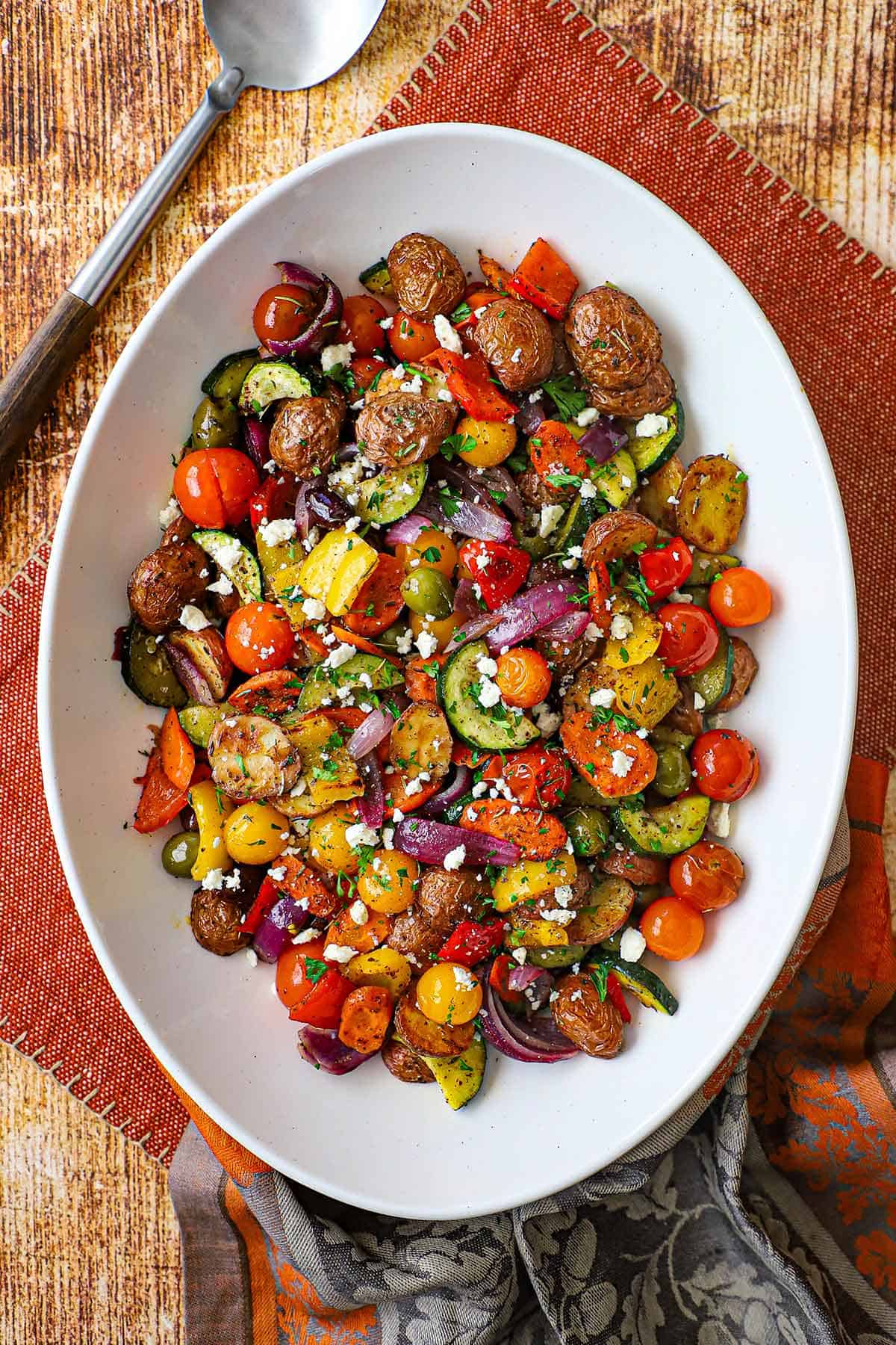 A large white platter filled with Mediterranean Roasted Vegetables topped with crumbled feta cheese and chopped Italian parsley.
