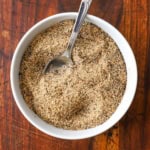 A small white bowl filled with Beef Rub with a spoon in the middle of it while the bowl is resting on a wooden cutting board.