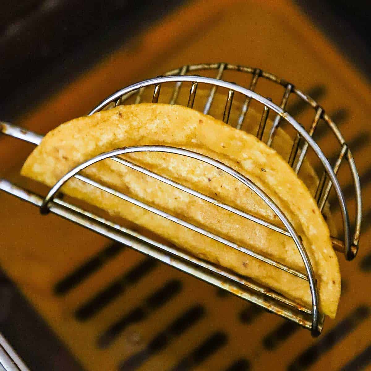 A person holding up a freshly fried taco shell in a metal taco shell mold.