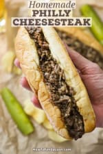 A person holding an uneaten, freshly prepared homemade Philly cheesesteak in his hand.