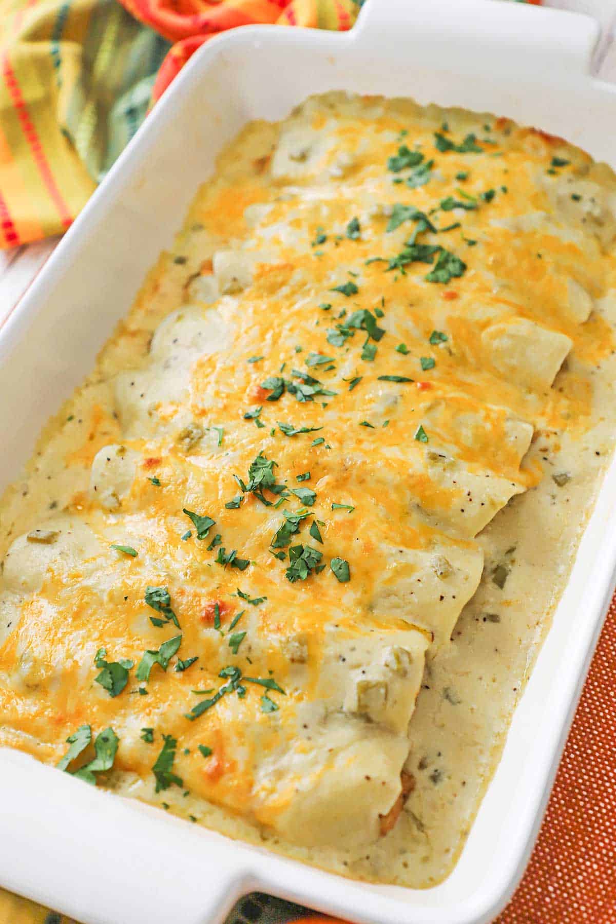 A nine by thirteen inch white casserole dish filled a row of chicken enchiladas with sour cream sauce.