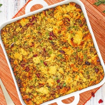 An overhead view of a square white baking dish filled with cornbread dressing and sausage and cranberries.