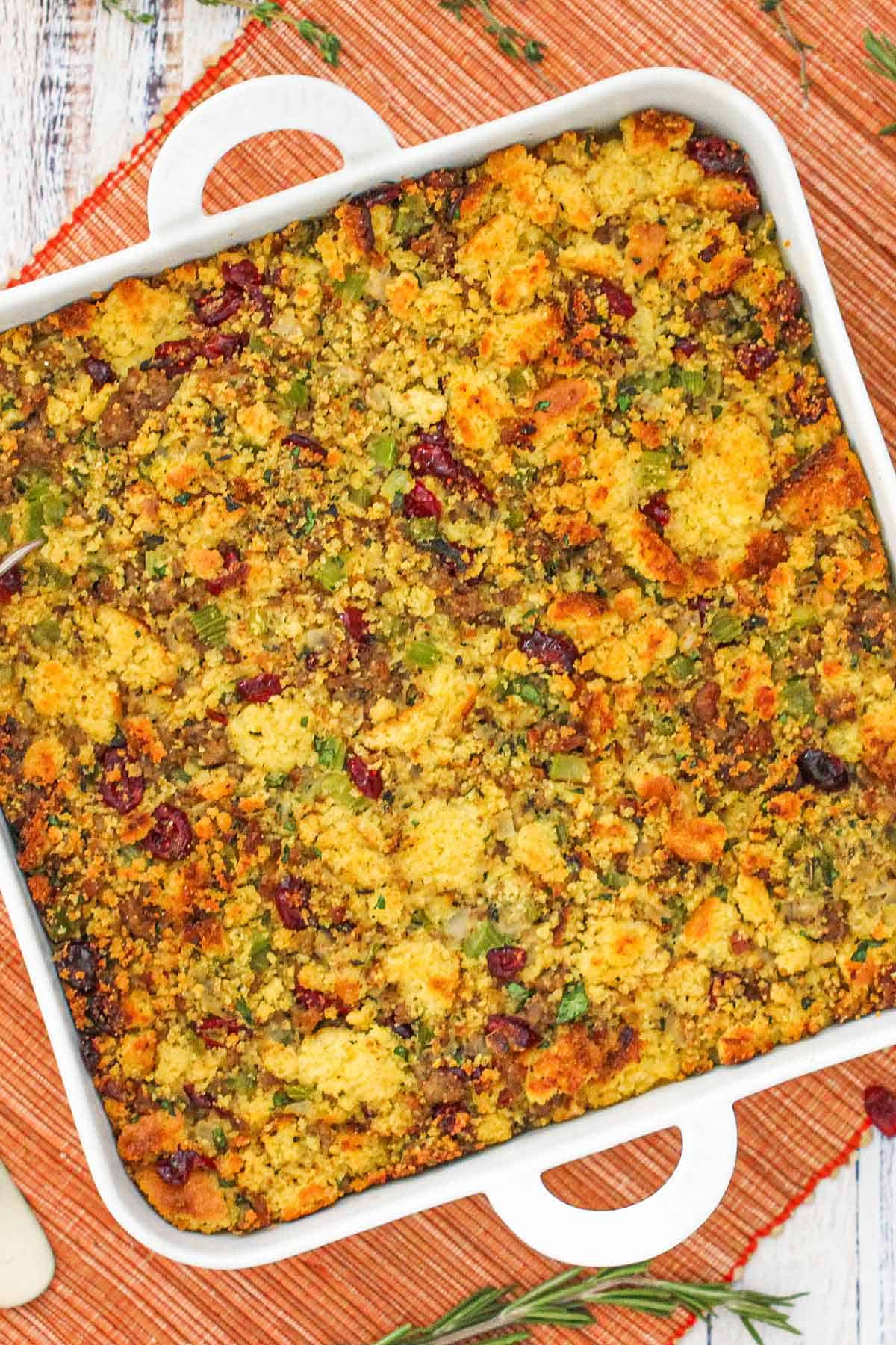 An overhead view of a square white baking dish filled with cornbread dressing and sausage and cranberries.