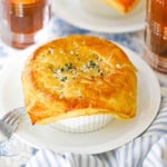 A close-up view of a leftover turkey pot pie with butter puff pastry in a large ramekin resting on a white dinner plate.