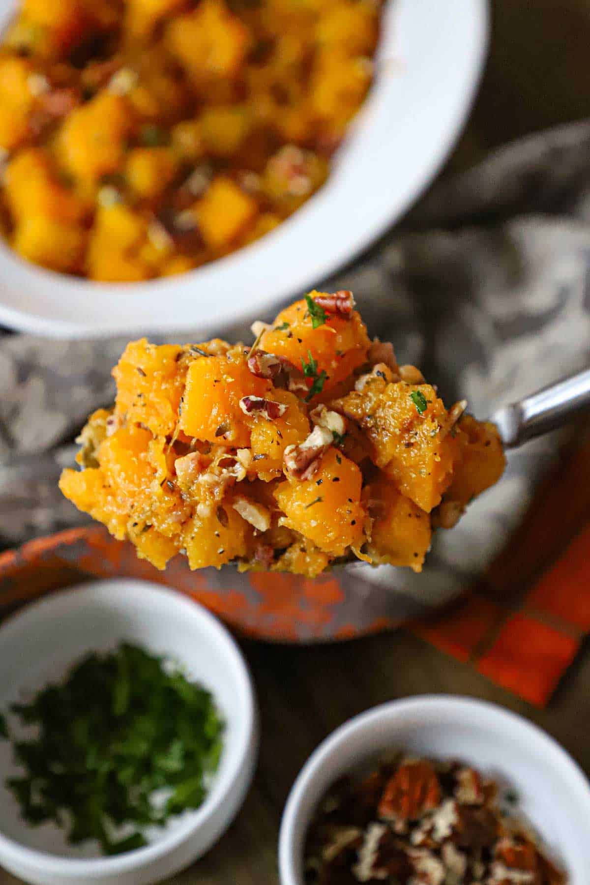 A person using a large serving spoon to hold up a mound of Maple-Glazed Butternut Squash with Pancetta and Herbs.
