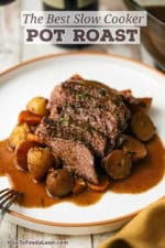 A white dinner plate filled with a serving of the best slow cooker pot roast with vegetables and brown gravy.