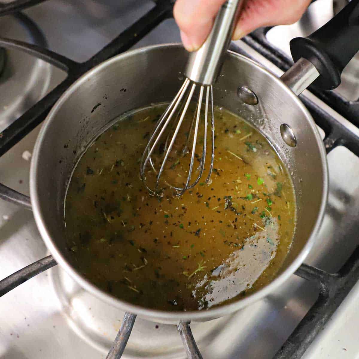 A person using a small whisk to whisk together a maple glaze that contains maple syrup, herbs, and seasonings.