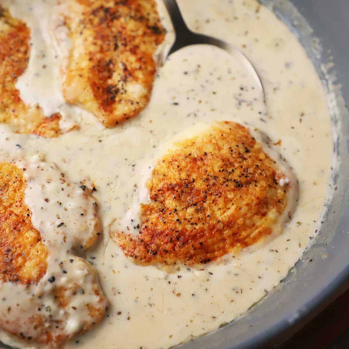 A close-up view of seared boneless chicken breasts resting in a creamy garlic parmesan sauce in a large non-stick skillet.