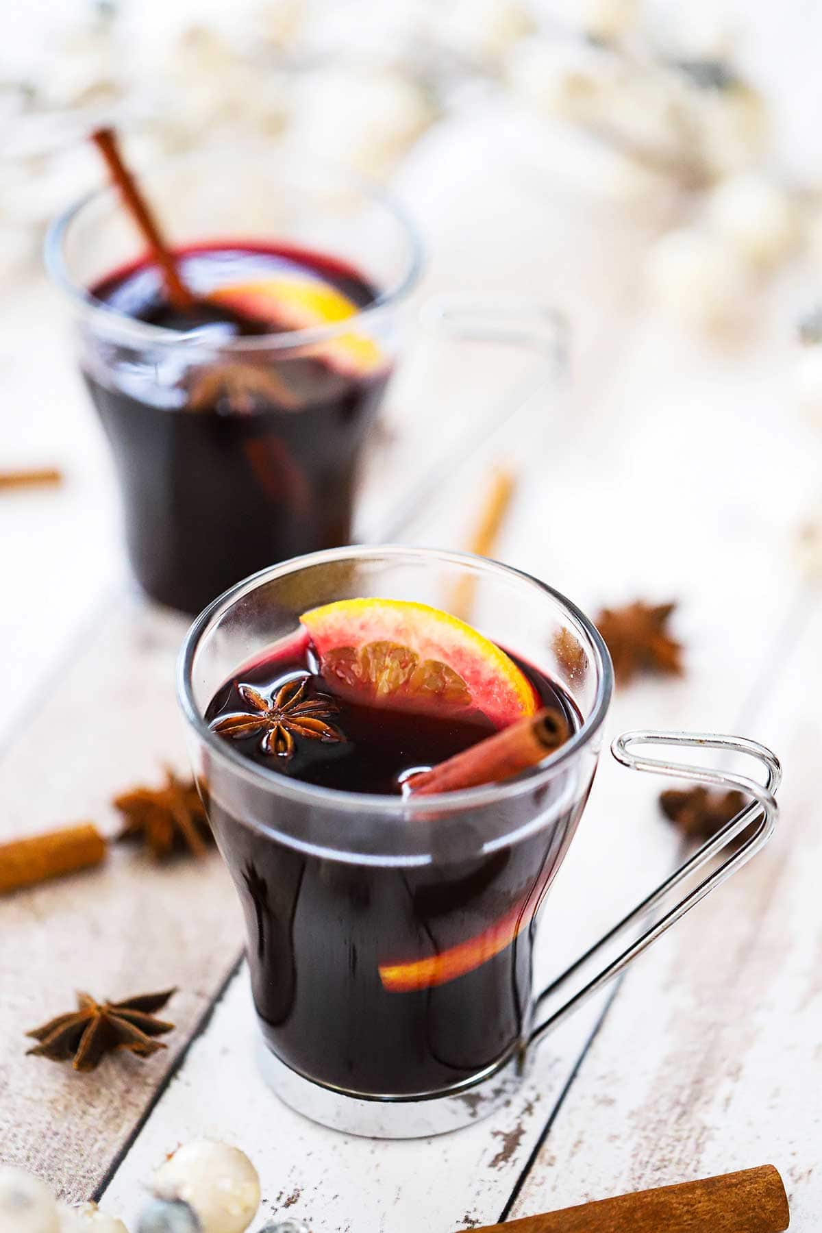 Two glass mugs filled with mulled wine (gluewein) garnished with an orange wedge, star anise, and a cinnamon stick.