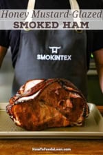 A person wearing a Smokin' Tex apron standing behind a honey mustard smoked ham that is resting on a sheet.