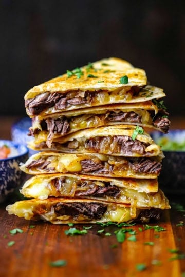 A stack of six steak fajita quesadillas that have been cut in half, revealing the steak, caramelized onions, and melty Monterey Jack cheese.