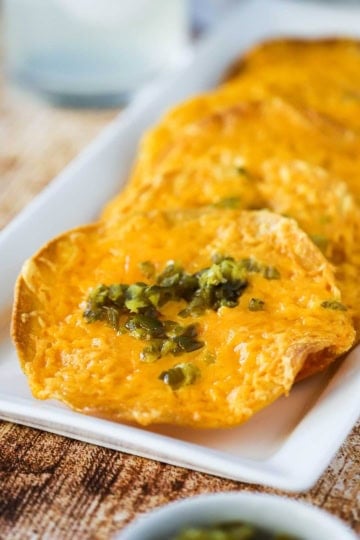 A rectangular white serving platter filled with a serving of classic nachos topped with chopped jalapeños.