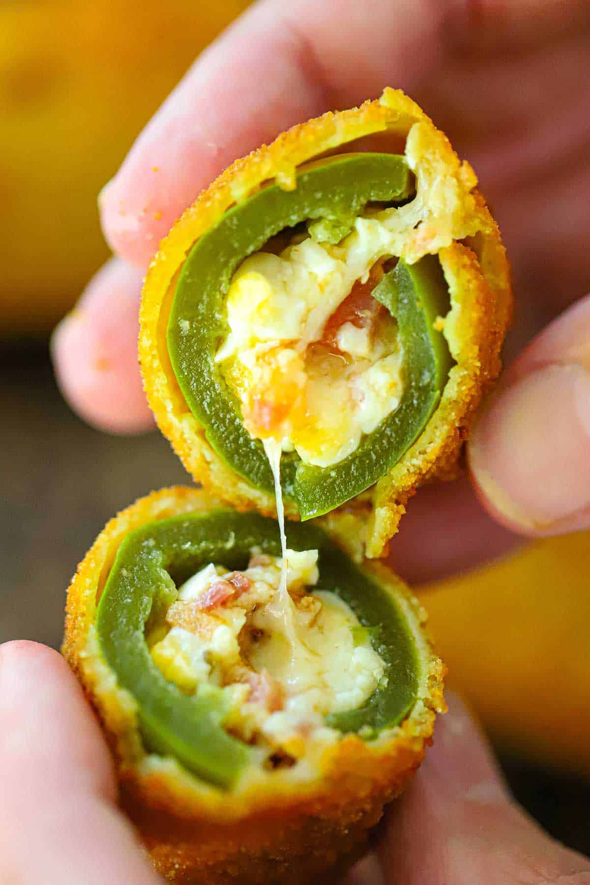 A person holding a jalapeño popper that has been split in half in the inside of the breaded is revealed showing melty cheese and pieces of crispy bacon.