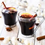 Two glass mugs filled with mulled wine (gluewein) garnished with an orange wedge, star anise, and a cinnamon stick.