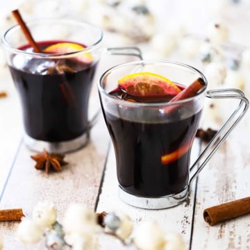 Two glass mugs filled with mulled wine (gluewein) garnished with an orange wedge, star anise, and a cinnamon stick.