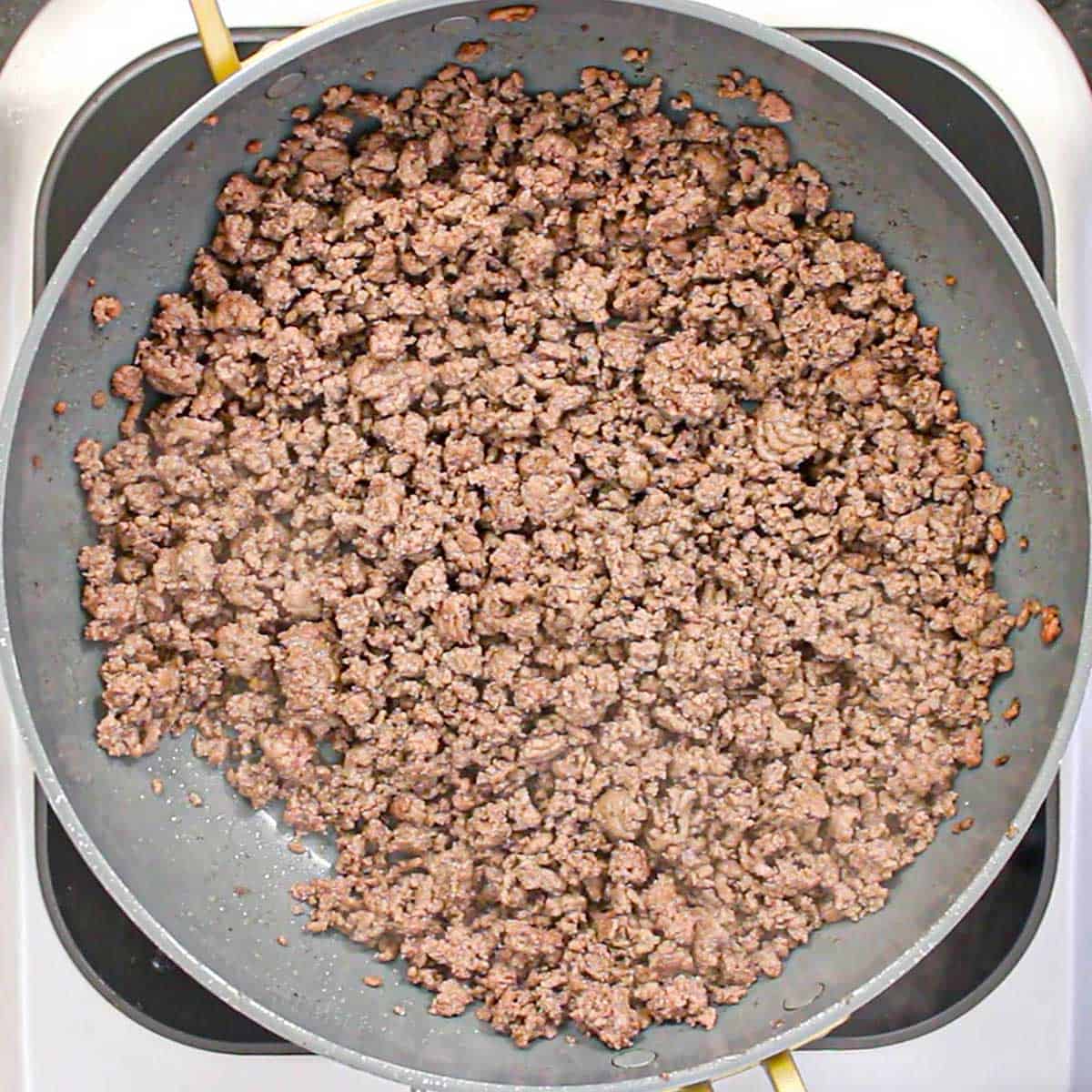 A large non-stick skillet filled with cooked ground beef on a portable induction stove.