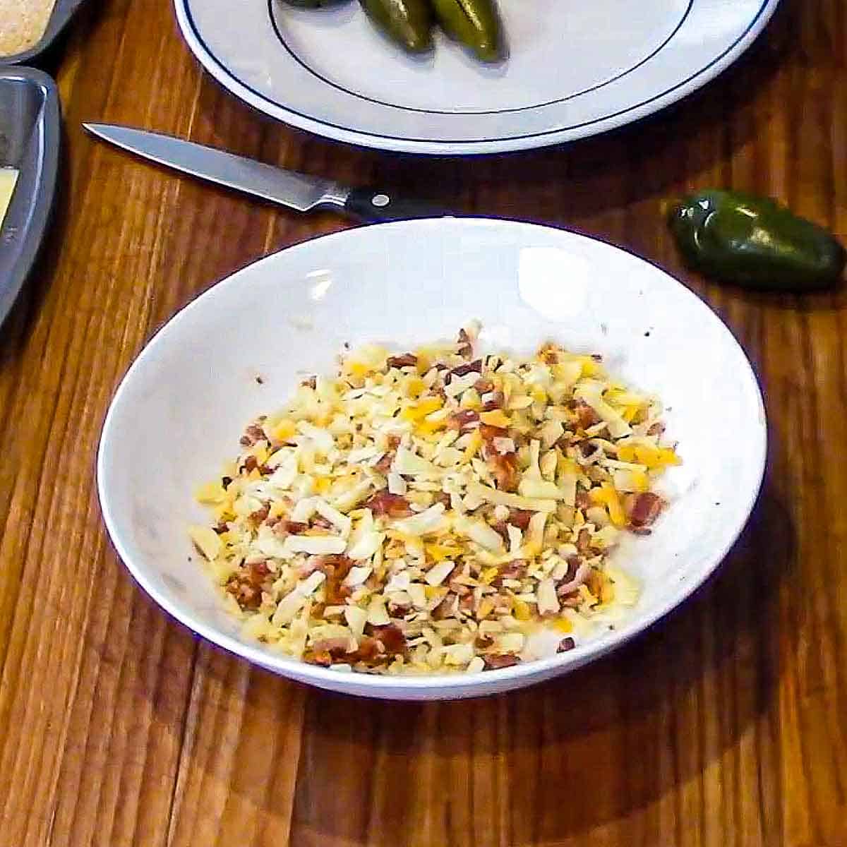 A white bowl filled with shredded Monterrey Jack cheese, cheddar cheese, and crumbled crispy bacon.