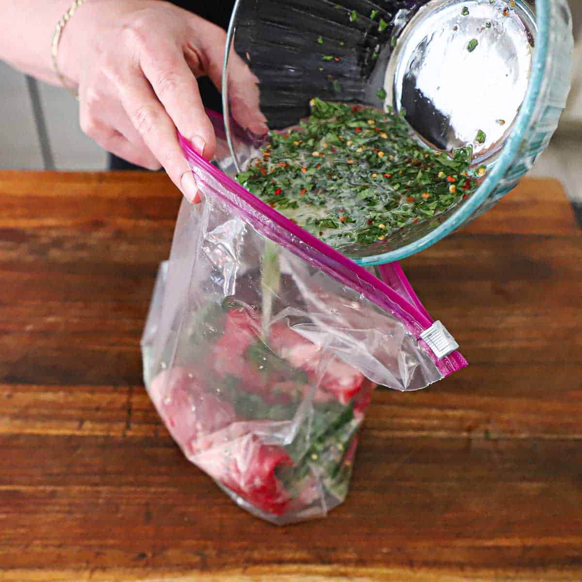 A person pouring a cilantro and lime marinade into a freezer baggie holding a skirt steak.