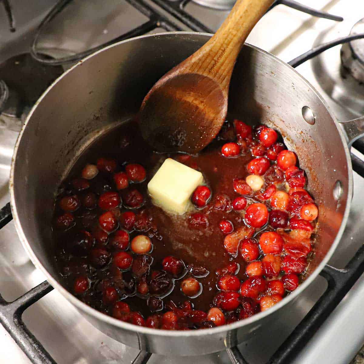 A saucepan filled with a cranberry-orange sauce with a pad of butter melting in the center of it.