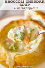 A spoon being used to raise a spoonful of broccoli cheddar soup over a bread bowl filled of the same.