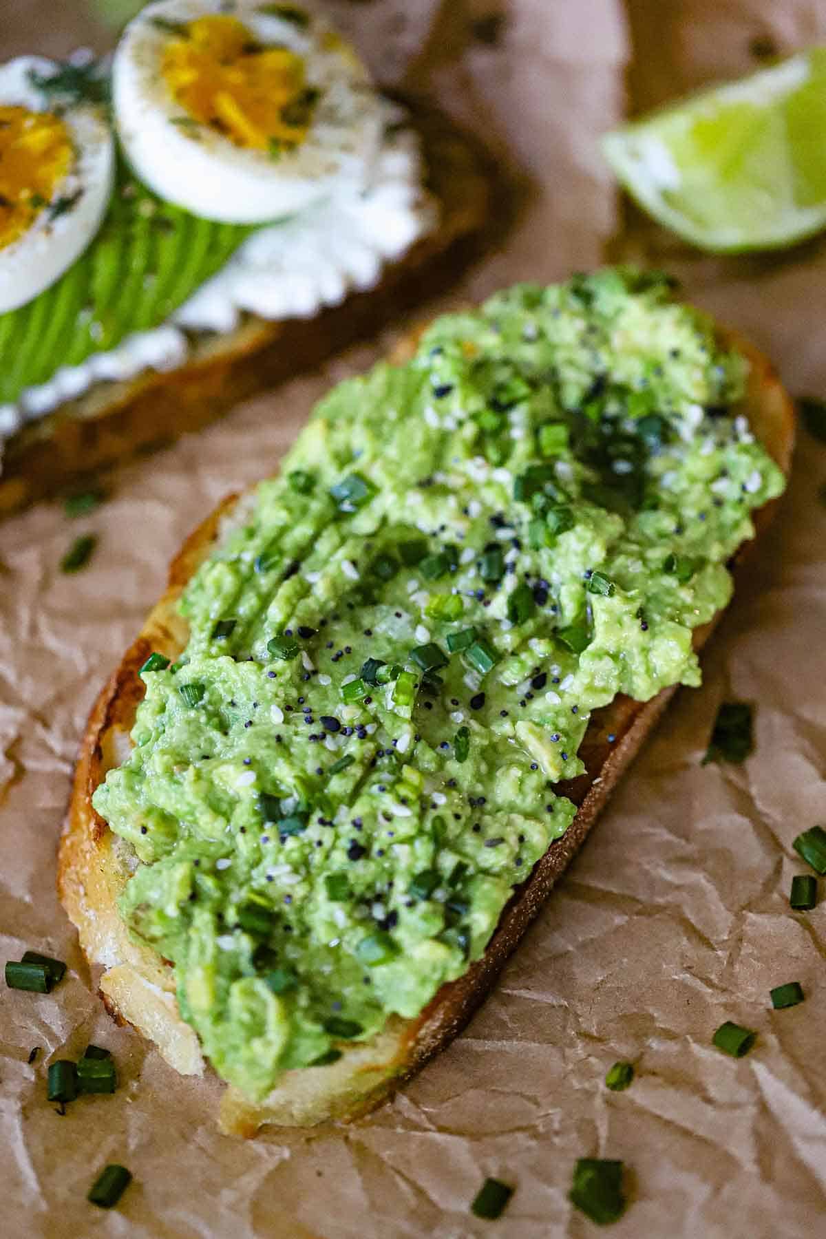 A close-up view of a classic avocado toast with freshly smashed avocado spread onto a toasted slice of sourdough bread and topped with seasonings and snipped chives.