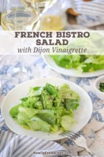 A close-up view of a white salad plate filled with a serving of a Classic French Bistro Salad topped with finely chopped herbs and freshly ground black pepper.