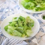 A close-up view of a white salad plate filled with a serving of a Classic French Bistro Salad topped with finely chopped herbs and freshly ground black pepper.
