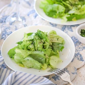 A close-up view of a white salad plate filled with a serving of a Classic French Bistro Salad topped with finely chopped herbs and freshly ground black pepper.