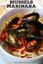 A close-up view of a bowl filled with cooked linguine topped with easy mussels marinara and garnish with chopped fresh basil.