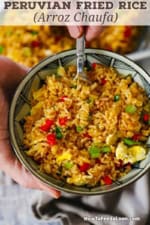A person holding a small serving bowl filled with Homemade Peruvian Fried Rice (Arroz Chaufa) in one hand and holding a fork inserted into the rice with the other hand.