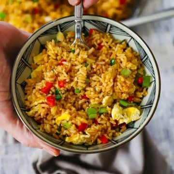 A person holding a small serving bowl filled with Homemade Peruvian Fried Rice (Arroz Chaufa) with a fork inserted into the rice.