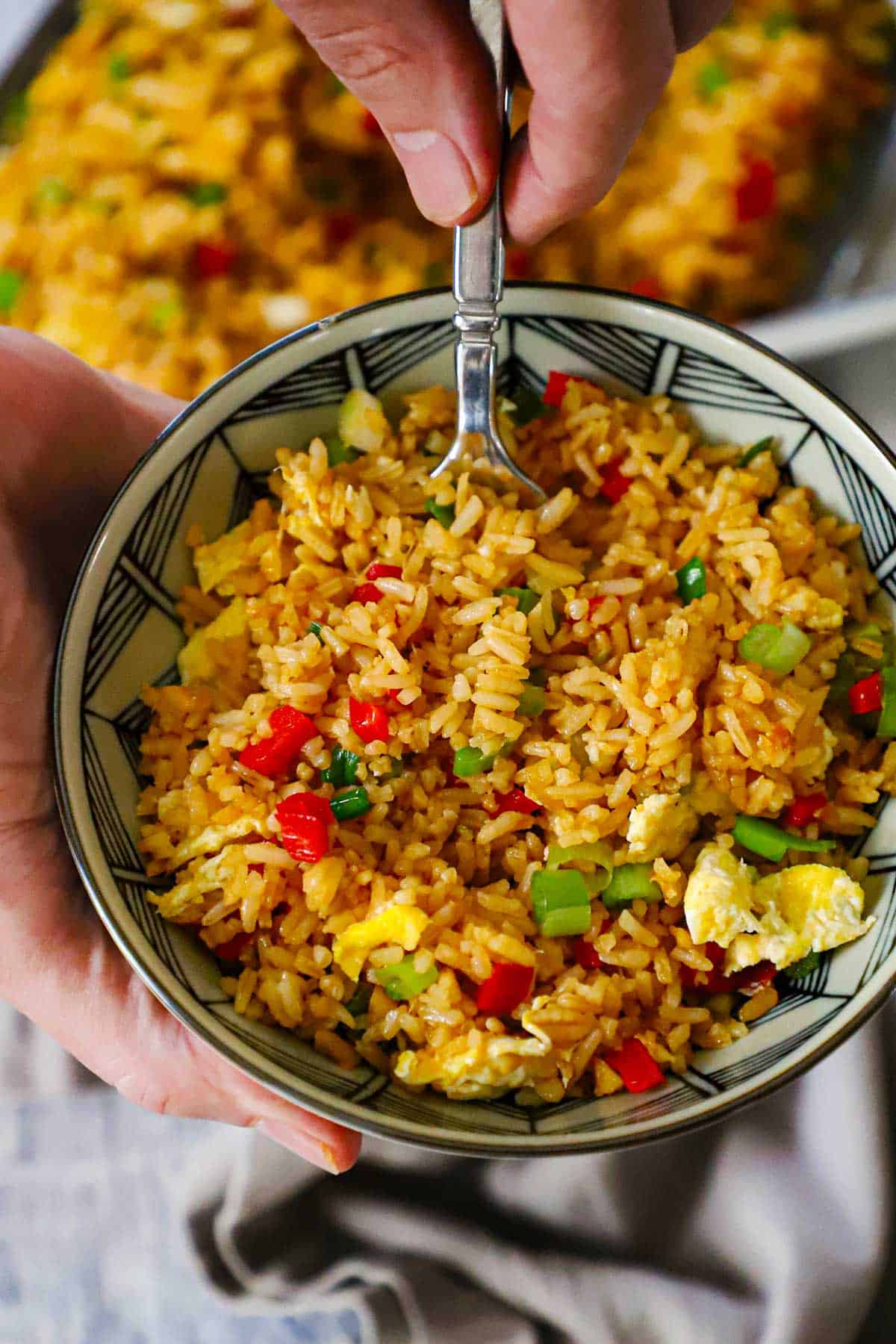 A person holding a small serving bowl filled with Homemade Peruvian Fried Rice (Arroz Chaufa) in one hand and holding a fork inserted into the rice with the other hand.