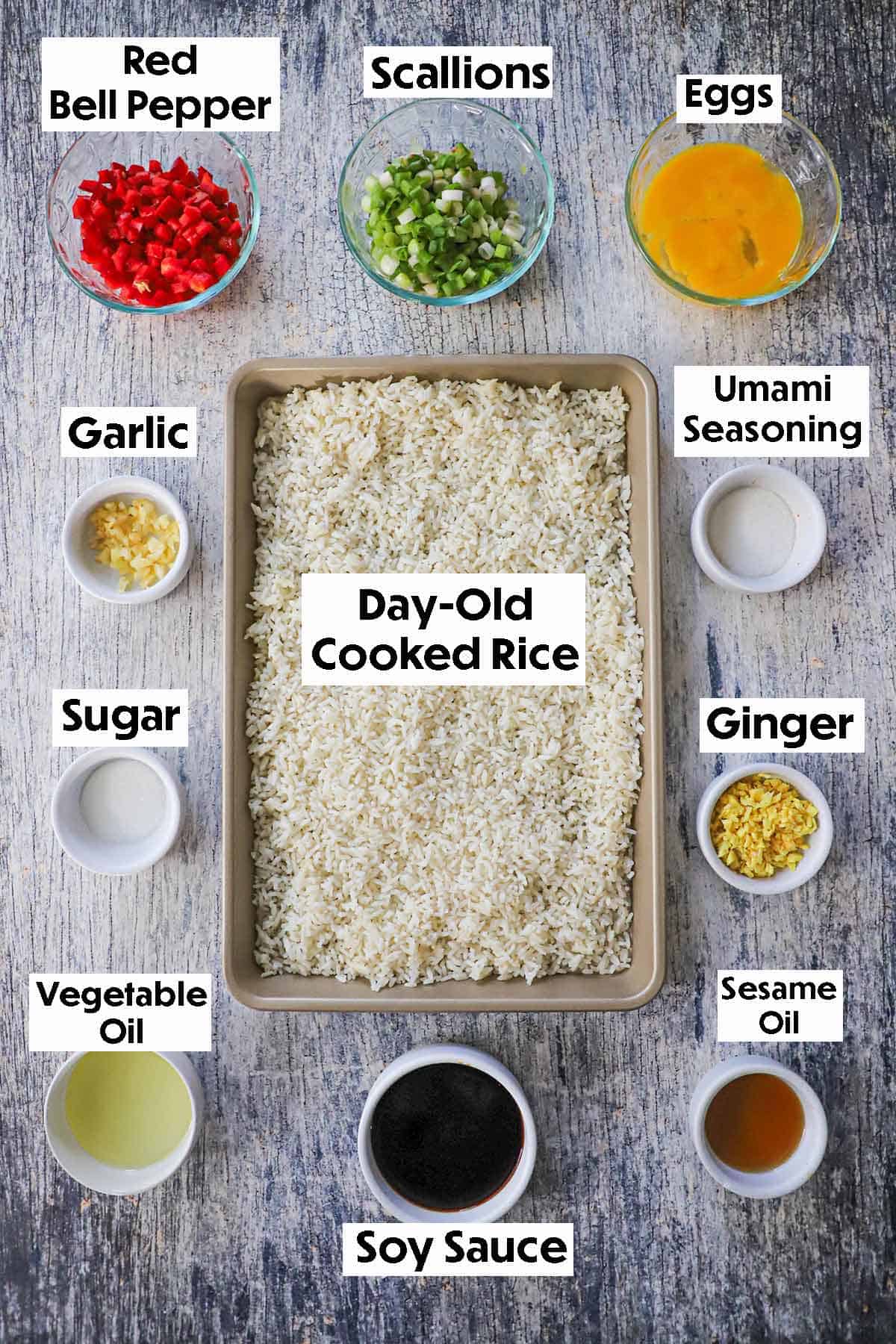 An arrangement of ingredients for Homemade Peruvian Fried Rice on a grey background including day-old cooked rice, red bell pepper, scallions, eggs, garlic, ginger, soy sauce, and seasonings.