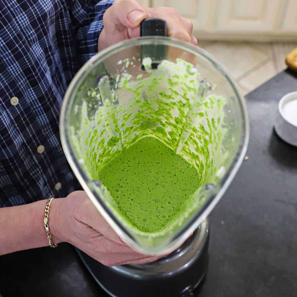 A person holding the main vessel from a blender to reveal a freshly puréed green sauce known as aji verde.