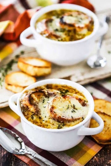 Two white soup bowl filled with homemade French onion soup with slices of a toasted baguette nearby.