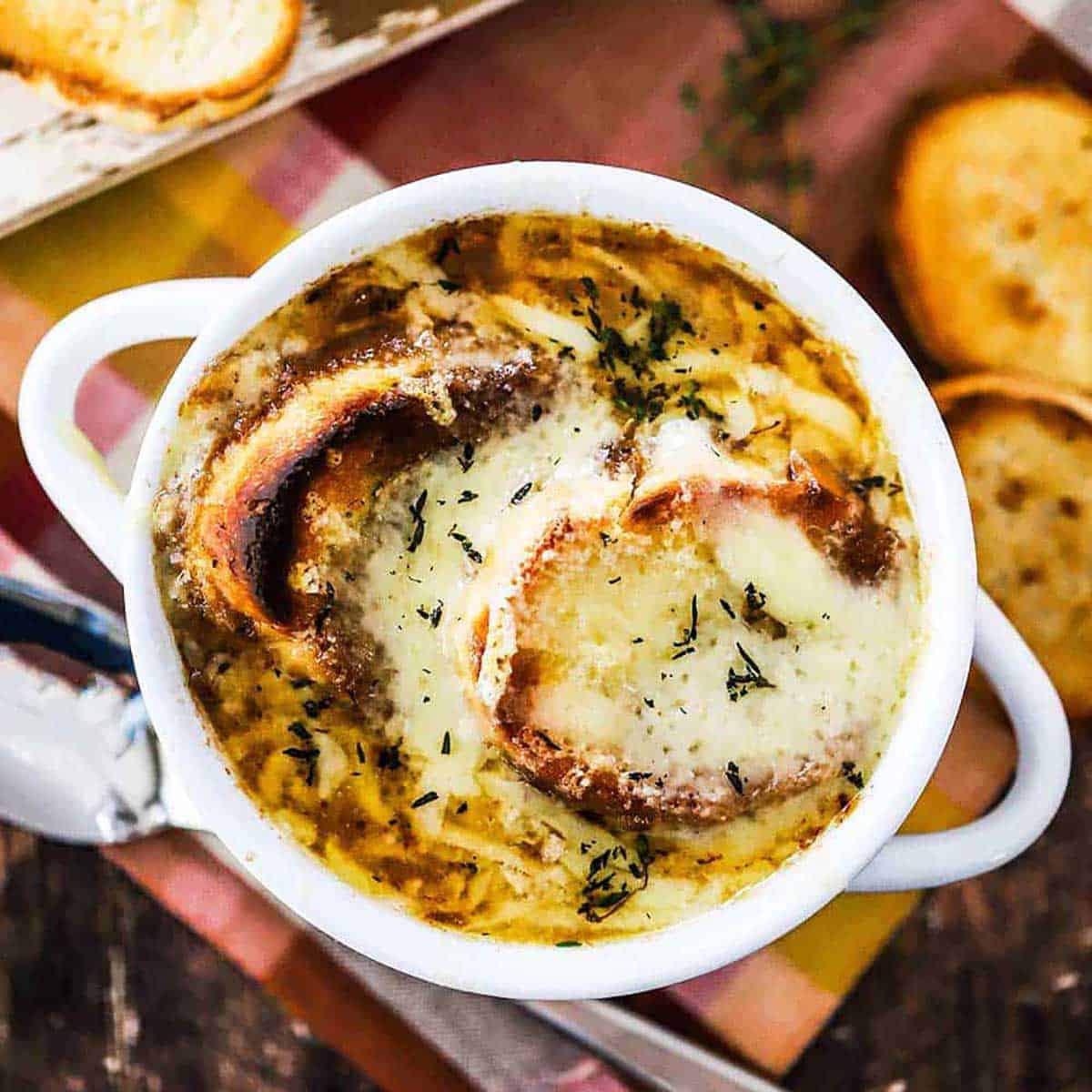 An overhead view of a soup bowl filled with homemade French onion soup with toasted baguette slices resting next to the bowl.