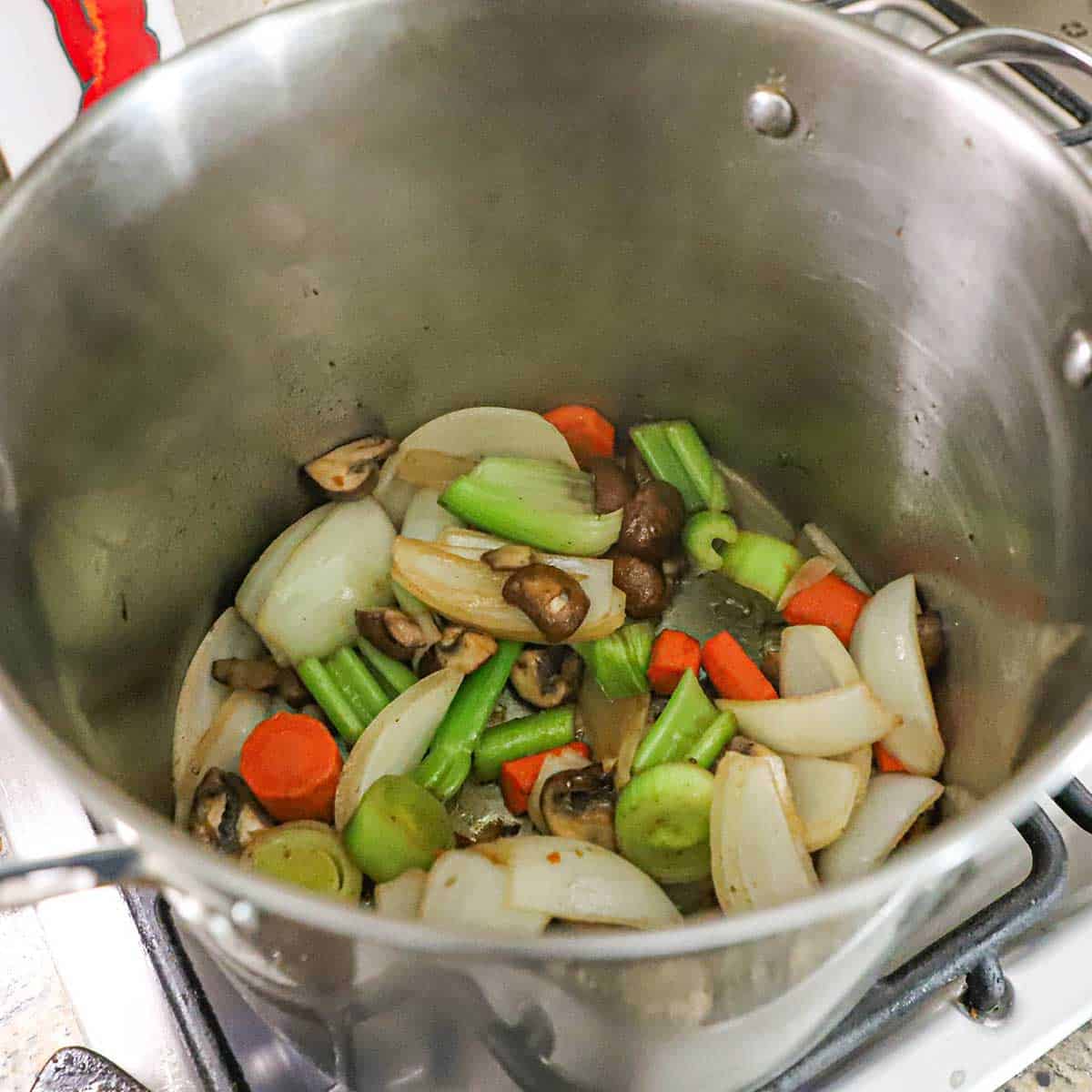 A view into a large stock pot that is filled with slightly charred vegetables and mushrooms.