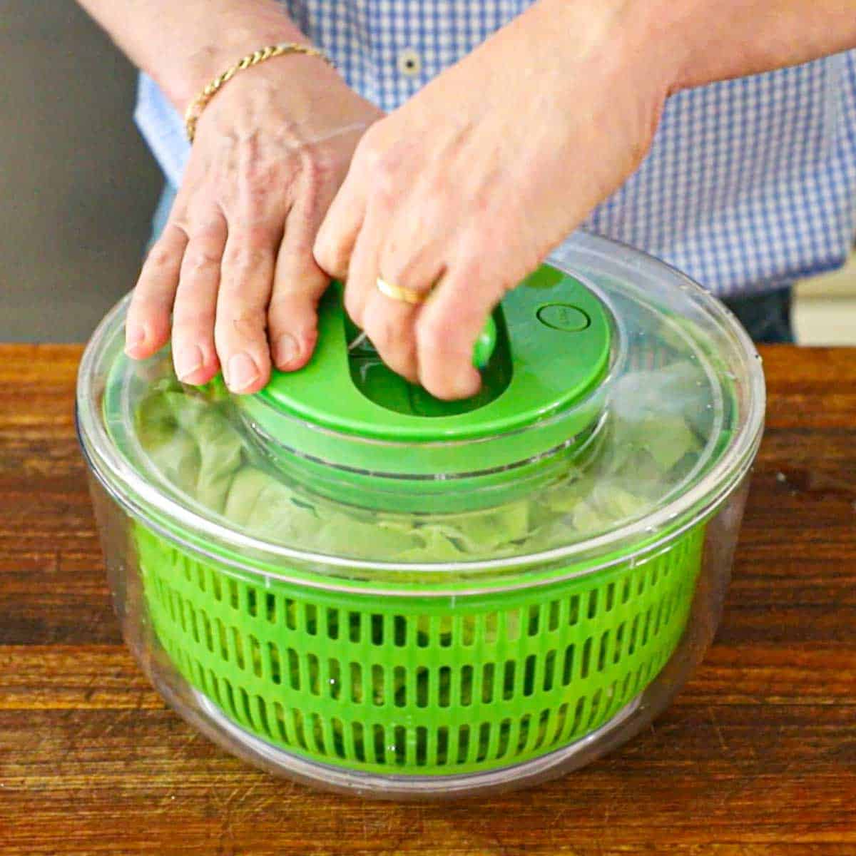 A person getting ready to pull the handle on the top of a salad spinner to dry the cut lettuce that is inside the spinner.