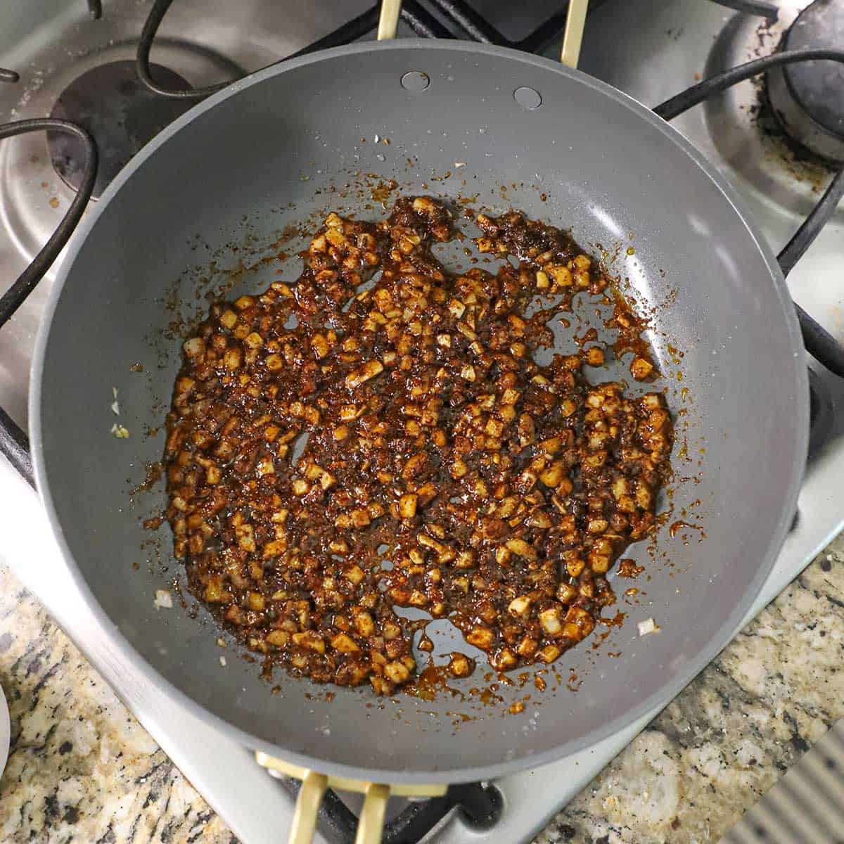 A large non-stick skillet filled with sautéed onions that are coated with chili powder and other seasonings on a gas stove.