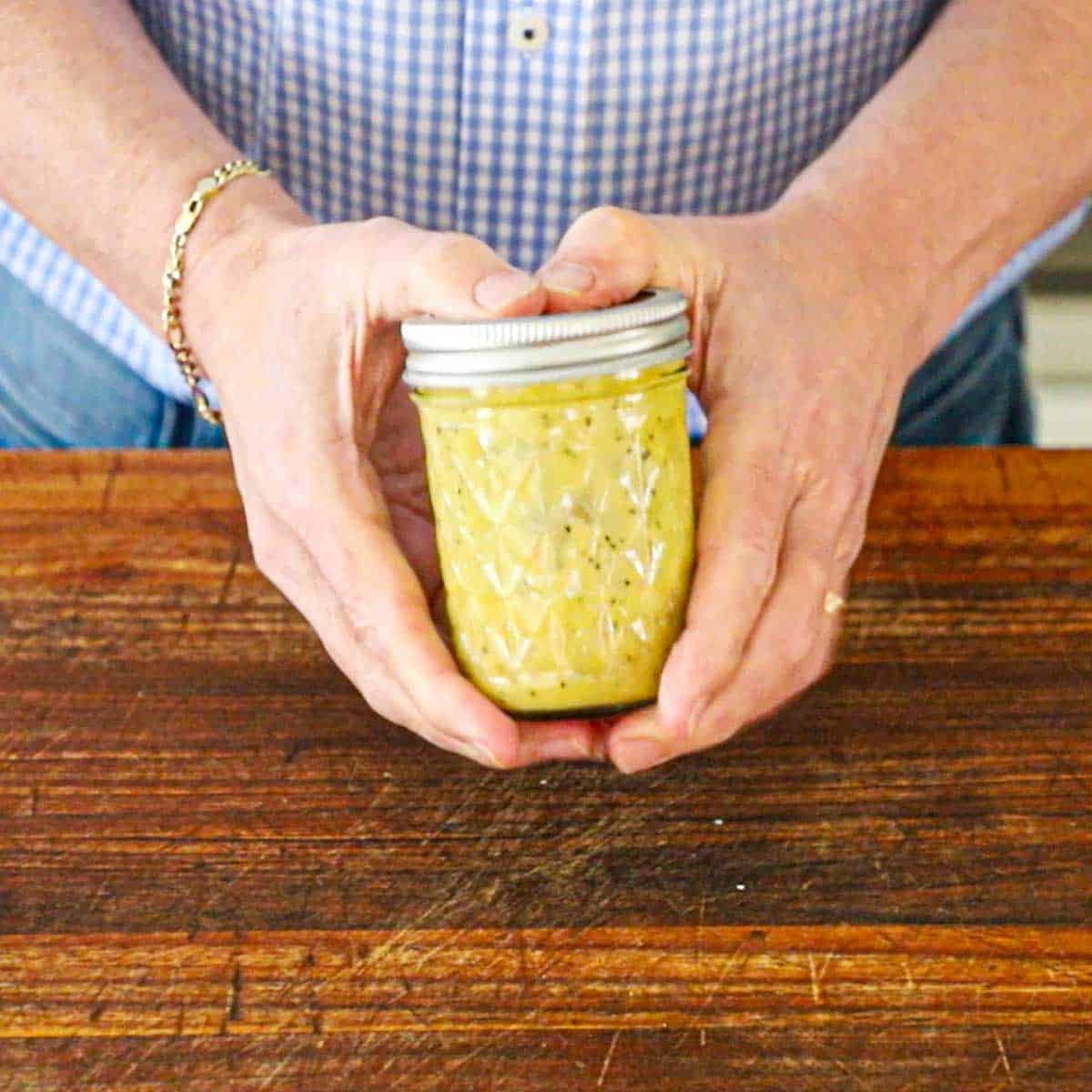 A person holding a small jar with an affixed lid that is filled with a French vinaigrette that has been emulsified.