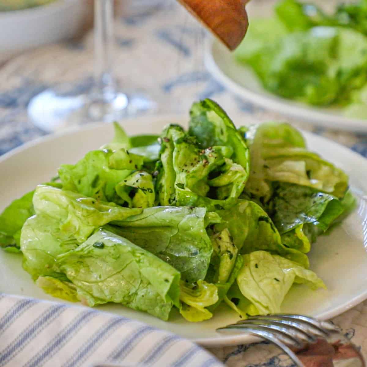 A person adding freshly ground black pepper from a pepper grinder onto a classic French bistro salad on a white salad plate.
