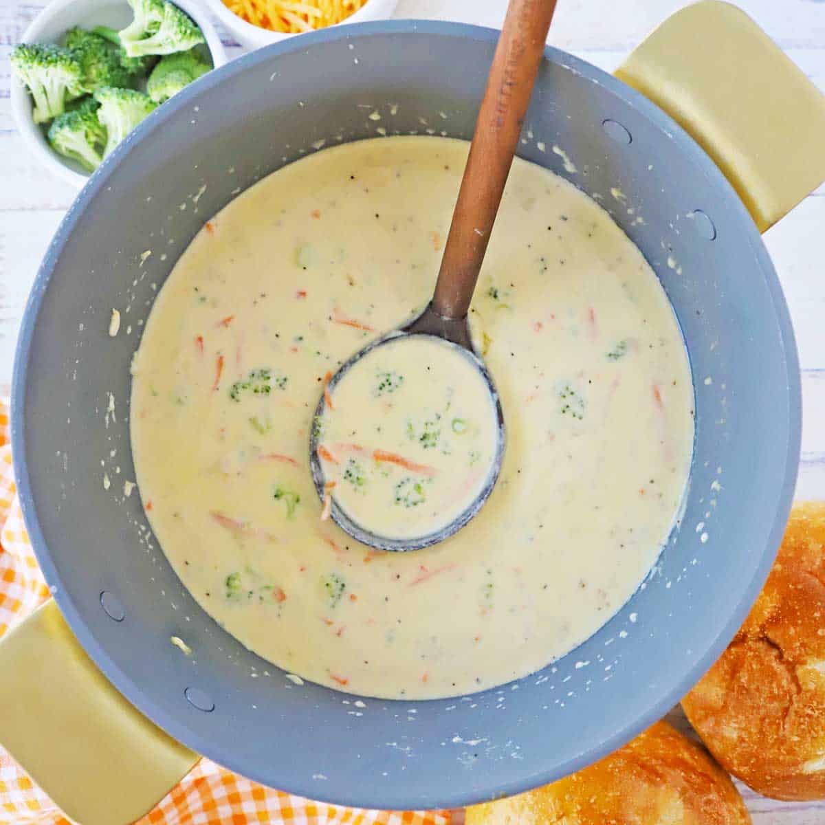 An overhead view of a large pot filled with cheddar broccoli soup (Panera copycat) with a wooden ladle in the middle of the soup.