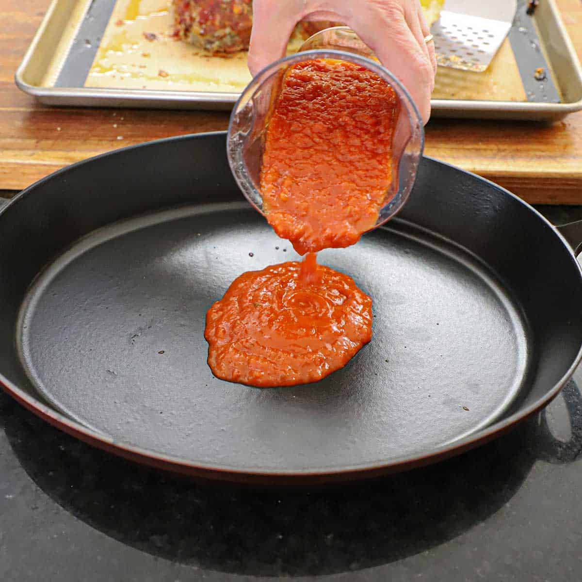 A person pouring homemade marinara sauce from a clear measuring up into an oval baking dish.